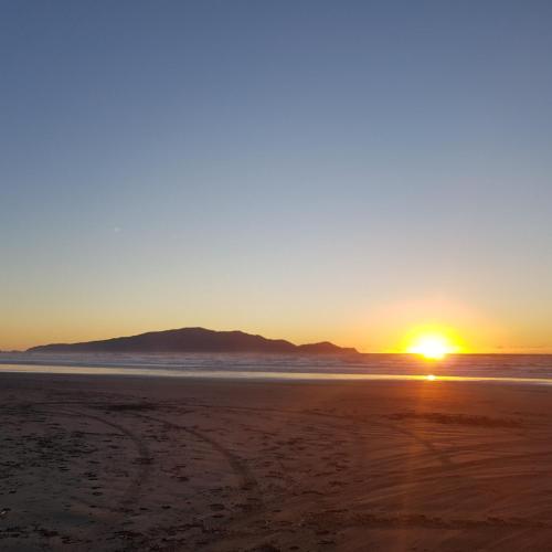 怀卡奈Near the shore的海滩上的日落,背景是山