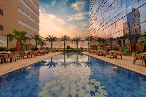 麦加Holiday Suites Al Azizia的酒店大楼前的带桌椅的游泳池