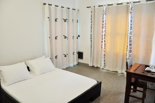 科托努Villa Ekabo的卧室配有白色的床、书桌和窗帘