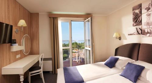波尔托罗Hotel Mirna - Terme & Wellness Lifeclass的酒店客房设有两张床、一张书桌和一个阳台。