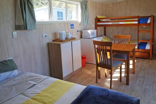 NgawiWaimeha Camping Village的一间卧室配有一张床、一张桌子和一张双层床。