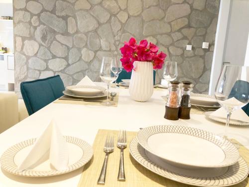 新阿尔塔基Colours Seaview Apartment的一张桌子,上面有盘子,花瓶上有粉红色的花