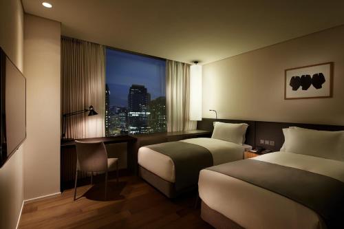 首尔Shilla Stay Gwanghwamun Myeongdong的酒店客房设有两张床、一张书桌和一个窗户。