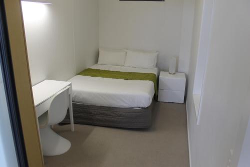 奥克兰曼努考中心公寓的一间白色的小卧室,配有一张床和一张书桌