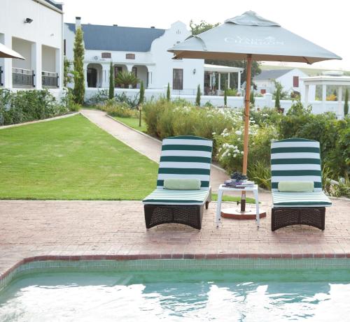 惠灵顿Val Du Charron Wine & Leisure Estate的游泳池旁的两把椅子和一把遮阳伞