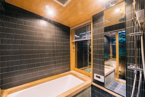 京都Miro Hachijo Genmachi Tei的浴室设有浴缸,铺有黑色瓷砖。
