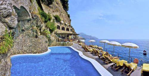 阿马尔菲圣塔卡特林纳酒店的毗邻大海的游泳池,配有椅子和遮阳伞