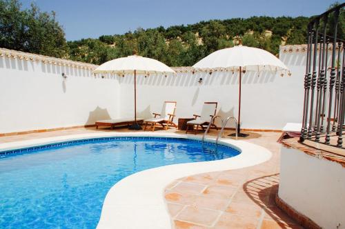 Villanueva de AlgaidasValle de Oro的一个带两把遮阳伞的游泳池和一个带桌椅的庭院。