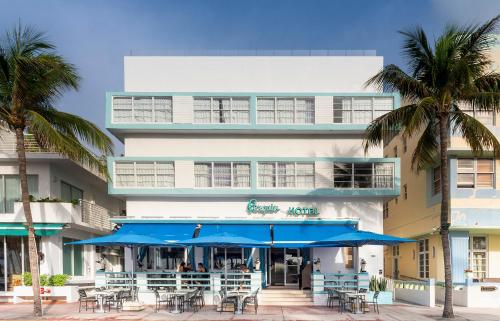迈阿密海滩企鹅酒店的一座配有桌子和蓝色遮阳伞及棕榈树的建筑
