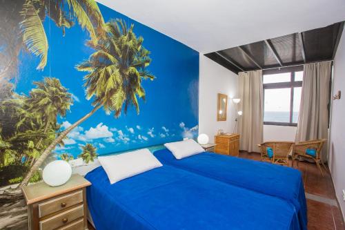 普拉亚布兰卡维斯塔马尔公寓的一间卧室配有一张蓝色的床,拥有棕榈树壁画