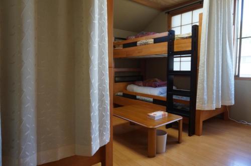 安昙野市Azumino Ikeda Guesthouse的客房设有两张双层床和一张桌子。