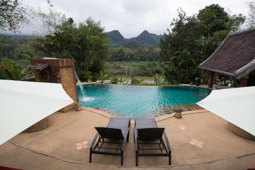 琅勃拉邦Shangri-Lao Resort的游泳池旁设有两把椅子,享有泳池美景