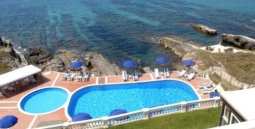 阿尔盖罗拉斯多洛娜斯温泉别墅酒店的毗邻大海的带椅子和遮阳伞的游泳池