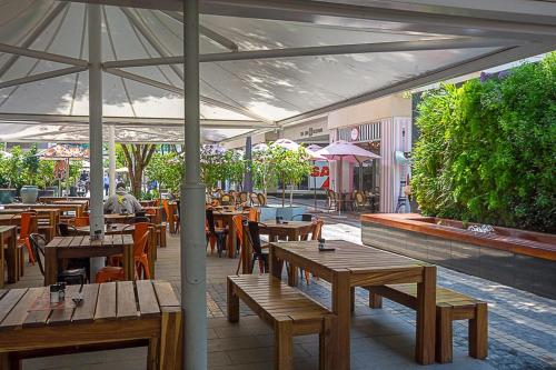 约翰内斯堡Hotel Amor Rosebank的一间带木桌和椅子以及遮阳伞的餐厅
