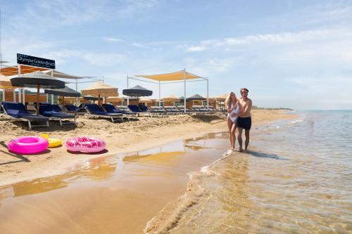基利尼奥林匹亚金海滩SPA度假酒店的站在海滩上的男人和女人