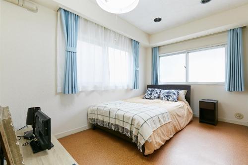 东京Haneda Lex House的一间卧室配有一张带蓝色窗帘的床和电视。