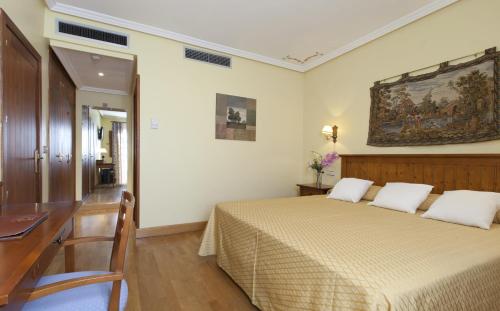 托莱多卡瑟纳香格里拉雷纳酒店的一间卧室配有一张带书桌的床,墙上挂有绘画作品