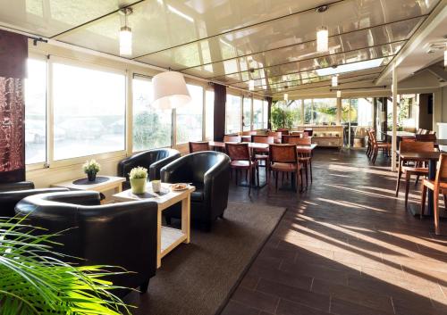 伊菲斯基里亚德南卡昂酒店的餐厅设有黑椅子和桌子以及窗户。