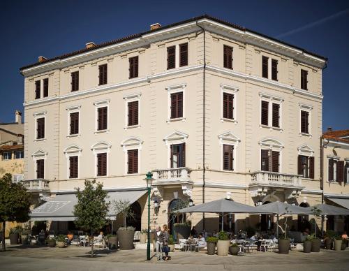 罗维尼Adriatic Hotel by Maistra Collection的一座白色的大建筑,前面设有桌子和遮阳伞