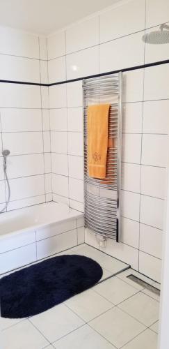 莫斯堡Haus Falkenstein的白色瓷砖浴室设有浴缸和橙色毛巾
