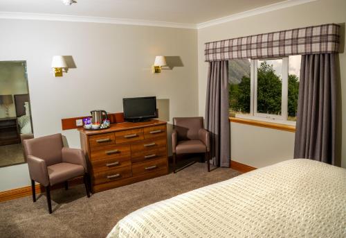 泰恩德拉姆Tyndrum Lodges的一间卧室配有一张床、两把椅子和电视
