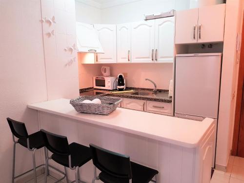 厄尔梅达诺Alquilaencanarias-Medano Colon Center, near the beach的厨房配有白色橱柜和带椅子的柜台。