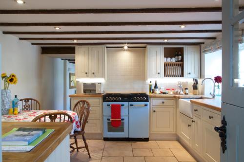 切达Strawberry Cottage的厨房配有白色橱柜和炉灶烤箱。