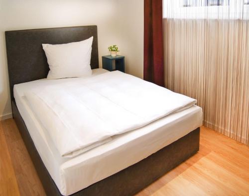 卡尔斯鲁厄SEEGER Living Premium West的一张带白色床单和黑色床头板的床
