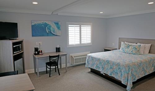 亨廷顿海滩冲浪城酒店的一间卧室配有一张床、一张书桌和一台电视
