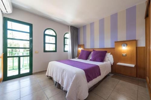 马斯帕洛马斯eó Maspalomas Resort的一间卧室配有一张带紫色枕头的大床