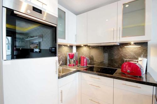 宾茨Villa Allegra的厨房配有白色橱柜和台面上的红色用具