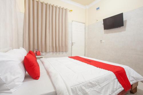 泗水RedDoorz Syariah At Sedati的一间卧室配有一张带红色枕头的床和电视。