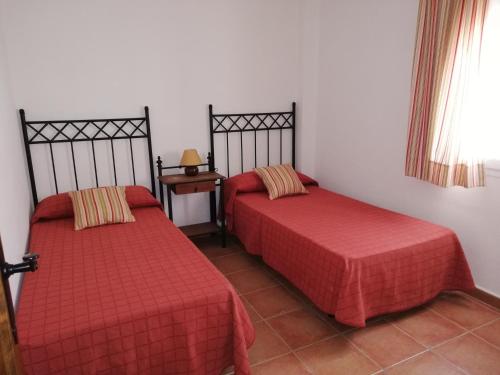 埃尔博斯克CASA HACIENDA EL OLIVAR的一间设有两张红色床单和一张桌子的房间