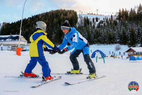 福尔加里亚Hotel La Baita的两个人在滑雪板上摇手在雪中