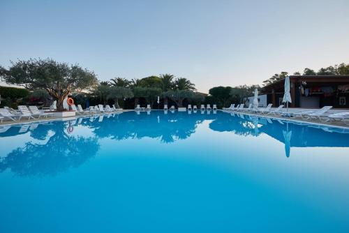 圣安德雷亚阿波斯托洛德洛约尼奥风之谷村酒店的一座带白色椅子和树木的大型游泳池