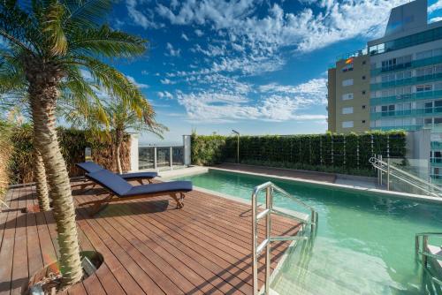 阿雷格里港Hotel Laghetto Stilo Higienópolis的棕榈树建筑中带游泳池的甲板