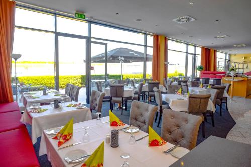 奥舍尔斯莱本赛车竞技场酒店的餐厅设有白色的桌椅和大窗户。