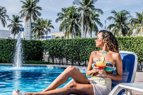 韦拉克鲁斯雅拉瓜酒店的坐在游泳池旁椅子上喝一杯的女人