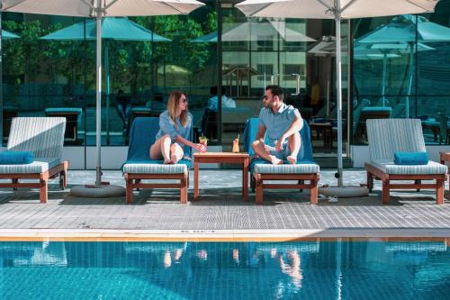 迪拜Stella Di Mare Dubai Marina Hotel的坐在游泳池旁椅子上的男女