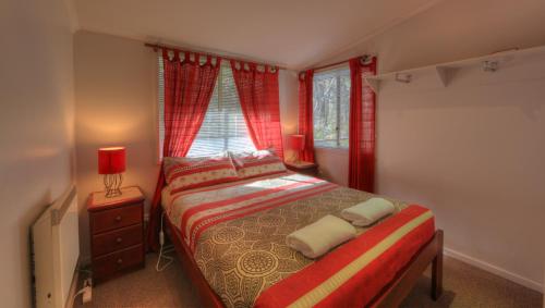 金德拜恩Kosciusko Tourist Park的一间卧室配有一张带红色窗帘的床和一扇窗户