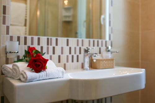 里米尼Hotel Bergamo的浴室的盥洗盆,毛巾上挂着红玫瑰