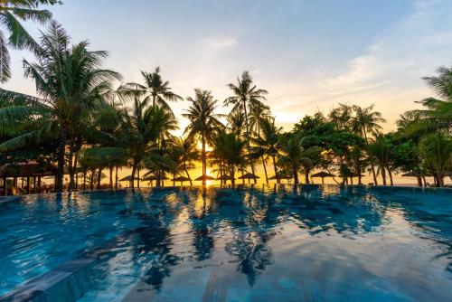 富国槟城侨海滩度假酒店的棕榈树和日落的度假村游泳池
