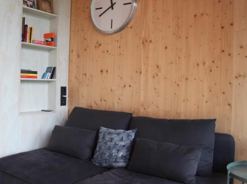 蒂尔堡ROOTS Tiny House的客厅配有沙发和墙上的时钟