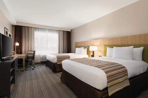 贝尔维尔Country Inn & Suites by Radisson, Belleville, ON的酒店客房设有两张床、一张桌子和一台电视。