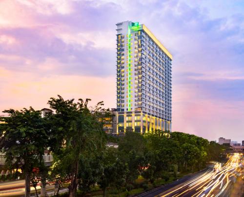 雅加达Holiday Inn & Suites Jakarta Gajah Mada, an IHG Hotel的一座高大的建筑,上面有绿灯