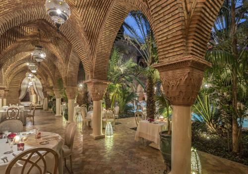 马拉喀什马拉喀什苏丹娜世界小型豪华酒店的棕榈树间内的餐厅,配有桌椅