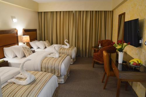 安曼Saray Hotel Amman的酒店客房设有三张床、一张桌子和一台电视。