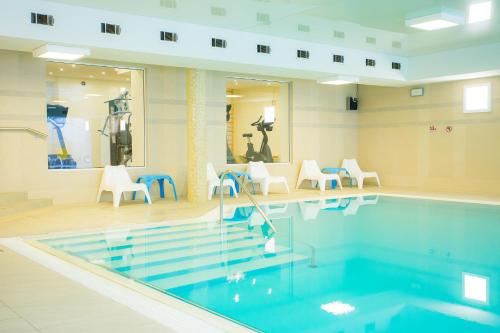 耶莱尼亚古拉Hotel Cieplice MEDI & SPA的游泳池,位于带白色椅子的房间