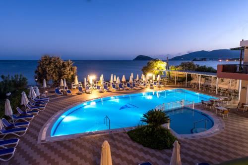 拉加纳斯地中海海滩度假酒店的一个带椅子和遮阳伞的游泳池,晚上则享有海景