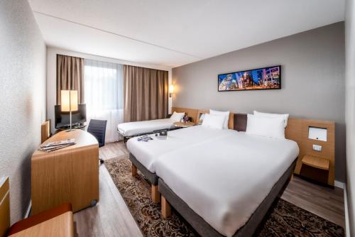 布雷达布雷达诺富特酒店的酒店客房设有一张大床和一张书桌。